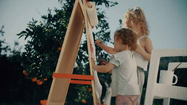 Two little girls paint outdoor in the garden
