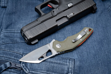 Folding tactical knife and pistol on jeans, close-up photo.