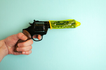 hand holds a gun dressed in a yellow condom on a blue background, the concept of erection, concept...
