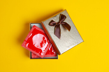 condom in a gift box on a yellow background, sexy gift, safe sex concept for the holiday