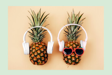 Two pineapples in sunglasses with headphones on light green and yellow background. Summer concept. Top view, flat lay