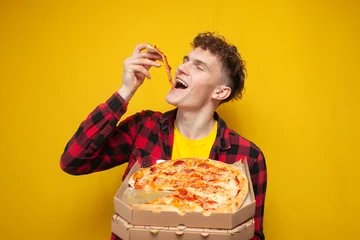 Deurstickers curly guy eating pizza on yellow background, hungry student enjoy fast food © Богдан Маліцький