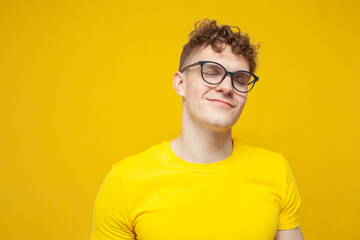 portrait of a young curly guy in glasses and a yellow t-shirt on a yellow background