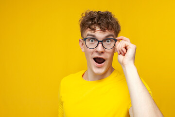 surprised guy student with curly hair holding glasses and looking, cute nerd in glasses on yellow...