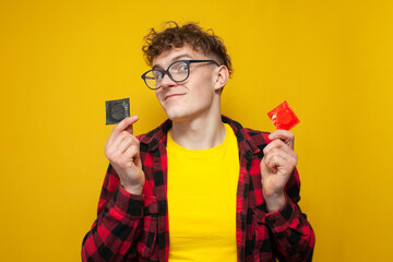 curly guy holds a condom on a yellow background and smiles, a student shows a contraceptive, the...