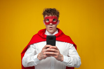 guy in a superhero costume uses a phone and shows surprise on a yellow background, super man holds...