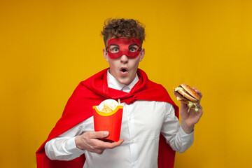 guy in a superhero costume eats a delicious burger and is surprised, man eats fast food, concept of...