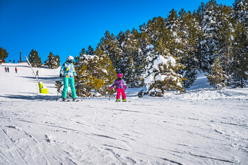 Mother and daughter skiing down a slope on a winter ski holidays in Andorra, El Tarter Snowy forest...