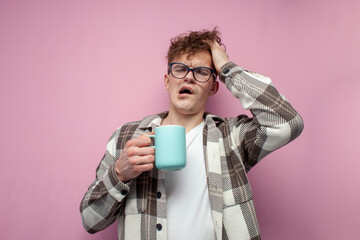 tired sleepy guy in glasses holds a mug of coffee and yawns on pink background, the concept of...