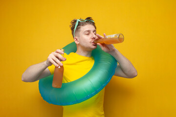 young guy on vacation in the summer drinks beer on a yellow background, a man with an inflatable...