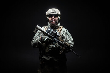 angry soldier in uniform with a rifle screaming at night, commando in stress on a black background,...