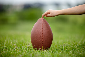 Child holder holding football for a kick by the placekicker laces away from viewer