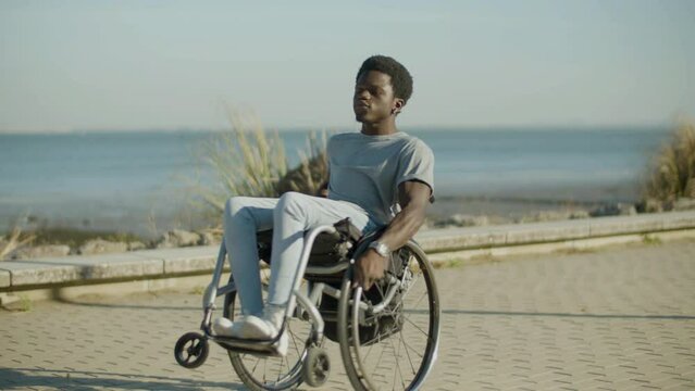 Young Black man in wheelchair having fun at seafront in city park. Happy energetic guy with paraplegia enjoying himself, spinning on wheelchair and singing. Happiness, motivation, disability concept.