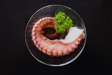 皿に載せた茹で蛸、ボイルしたタコ、蛸の切り身、茹でタコ、黒背景
