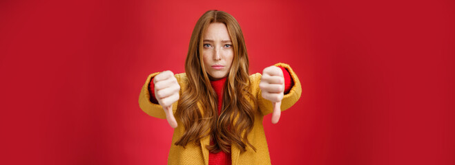 Portrait of insecure and unconfident cute redhead female reacting to uncool thing showing thumbs...