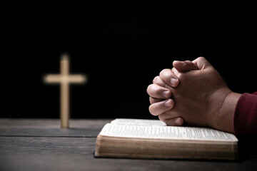Hands folded in prayer on Holy Bible with cross in church concept for faith, spirituality and...