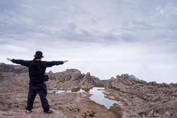 Latin man with open arms, looking out over the valley, with a lagoon and a valley of rocks in the background.