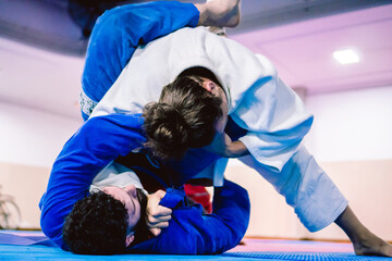 Young Latino and Hispanic male with beard applying a submission lock from the ground against his opponent in a jiu-jitsu practice.