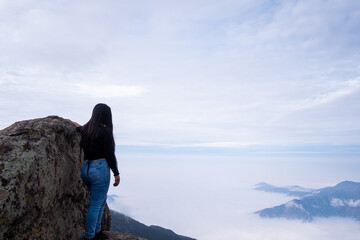 landscape where a latin woman sees a cushion of clouds, standing on the edge of a cliff in the Peruvian Andes.