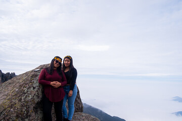 a lesbian couple taking a picture of themselves, on the edge of a cliff in the Peruvian Andes, to be able to see the cloud bed.