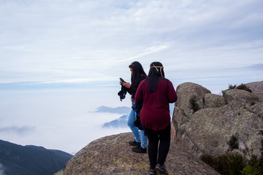 2 latina girls, walking to the edge of the cliff to take pictures with their cell phones of the cloud bed.