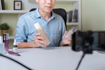 Young adult Asian beauty video blogger man filming, online live streaming his video blog about male cosmetic, male skincare. Guy looking camera to show new skin care for men product, teaching make up.