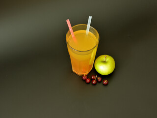 A tall glass of fruit juice with straws on a black background, next to ripe cherries and a green apple.