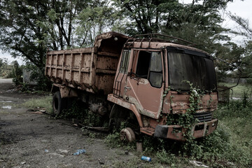 Fototapeta na wymiar Side view of a broken old truck that has been badly damaged abandoned in the middle of a park with scary vibes