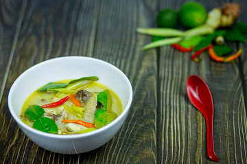 Thai Chicken Coconut Milk Soup a topping chili kaffir lime leaves serving hot on dark wooden table along with red spoon or thai person called Tom Kha Gai.