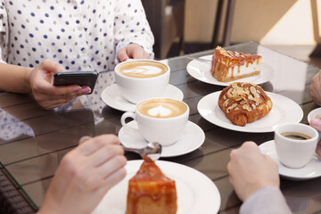 Friends drinking coffee at wooden table in outdoor cafe, closeup