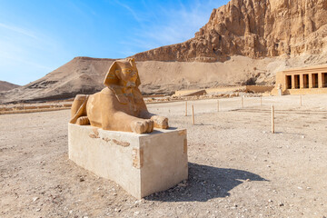 An Egyptian Sphinx lies in the desert sand in front of the Mortuary Temple of Queen Hatshepsut...