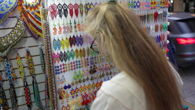 Mature woman tourist wearing ethnic clothes looking at locally made blouses in a souvenir shop in Merida, Yucatan, Mexico.