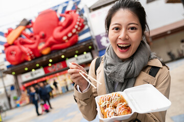 happy Asian Japanese girl looking at camera and showing takoyaki in box with a big octopus sign at...