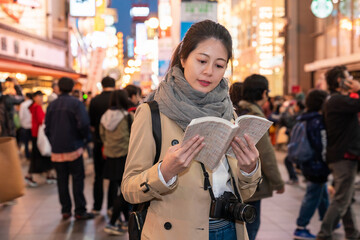 smiling Asian Taiwanese woman traveler looking at a guidebook for advice while visiting...