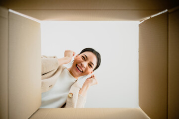 Surprised young asian woman unpacking. Opening carton box and looking inside. Packaging box,...