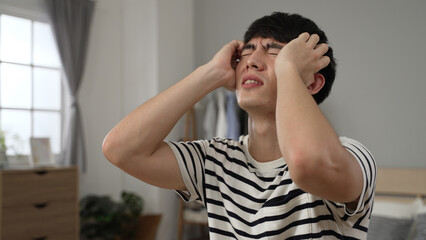 closeup shot of a frustrated asian Chinese young man working from home is holding his head in despair over an unexpected error on the computer device