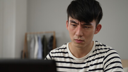 Obraz premium overworked Japanese young student having sudden blurry vision is rubbing his eyes while working from home on the computer.