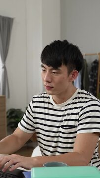 Vertical Screen: Asian Japanese male student learning from home is cheering with hand gesture and taking break with stretch while feeling happy about finishing school project on laptop