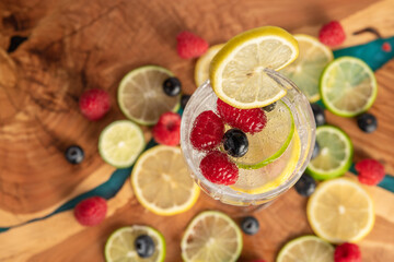 Club soda drink surrounded by lemon and lime slices and berries, horizontal