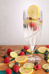 Club soda with fruit and lemon garnish in tall glass, surrounded by fruit with copy space