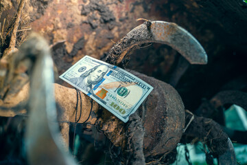 Hundred dollar bill on a dirty tractor rototiller close-up. Rotary tiller for tillage of...