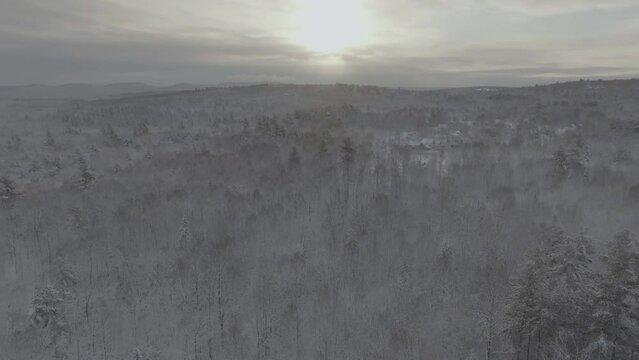 Aerial view above snow-covered forest sunlight breaks through clouds