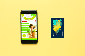 Mobile phone with opened page of online grocery shop and credit card on color background