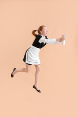 Fototapeta na wymiar Young female chambermaid with bottle of detergent jumping on beige background