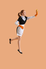 Fototapeta na wymiar Young female chambermaid with rag jumping on beige background
