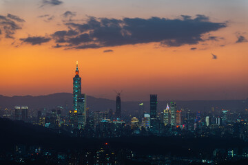 Fototapeta premium A vibrant cityscape with an orange night sky. Night view of the city surrounded by mountains is hazy and dreamy.. Taipei City, Taiwan