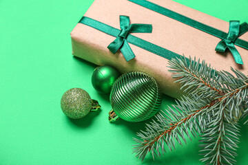 Composition with beautiful gift box, fir branch and Christmas balls on green background, closeup