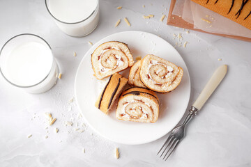 Plate with pieces of delicious sponge cake roll, fork and milk on white table