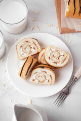 Plate with pieces of delicious sponge cake roll, fork and milk on white table