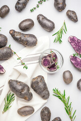 Composition with cut and whole purple potatoes and herbs on white background